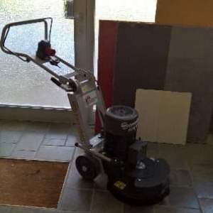 Bodenreinigungsmaschine mit Griff und Motor, steht auf gefliestem Boden vor einer Tür