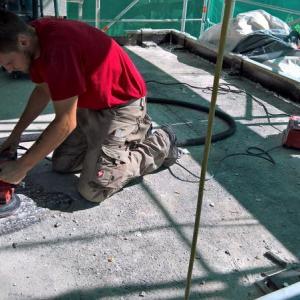 Mann kniet auf Boden und arbeitet mit Schleifmaschine auf Baustelle